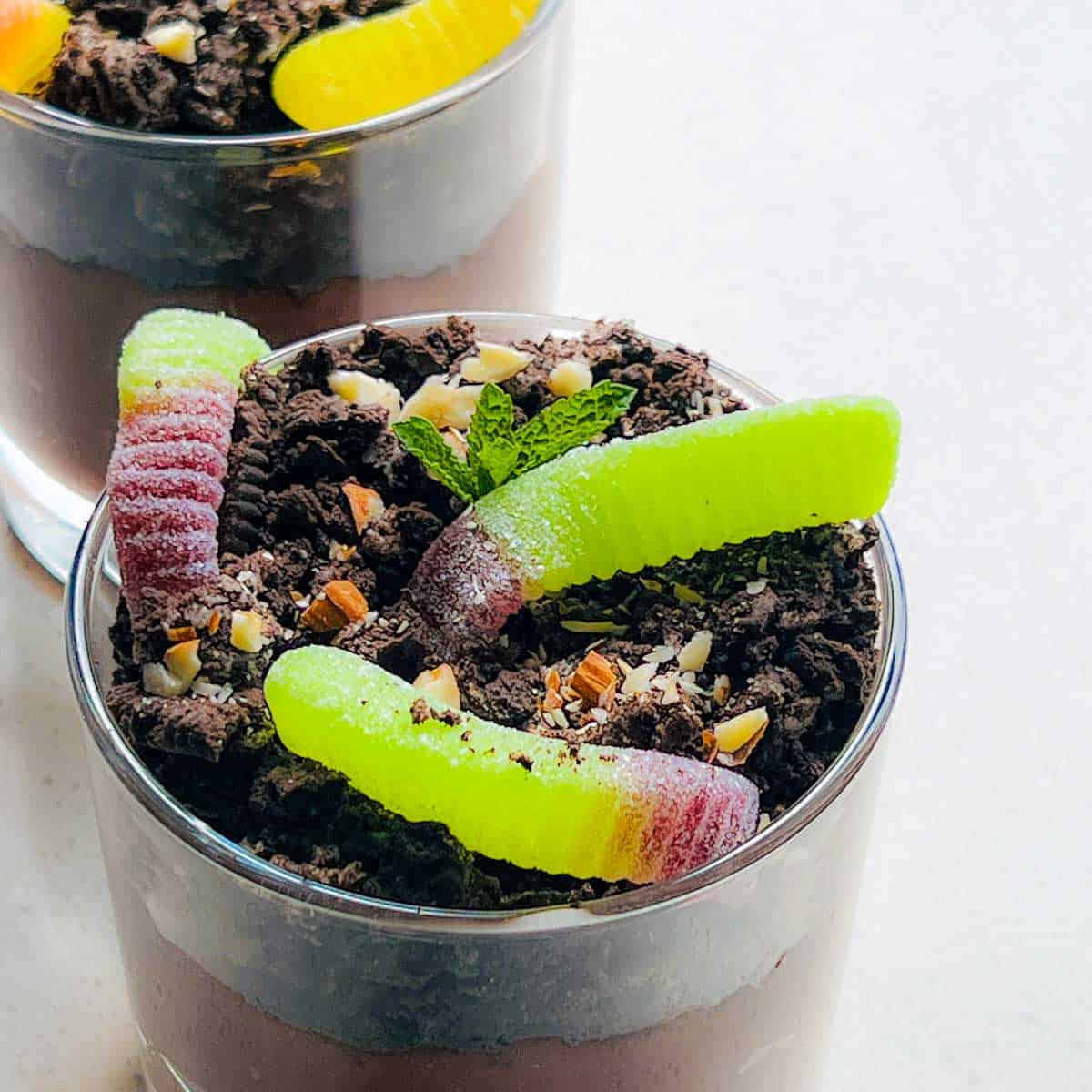 Pudding glasses topped with crushed orea, chopped almonds, and gummy worms.