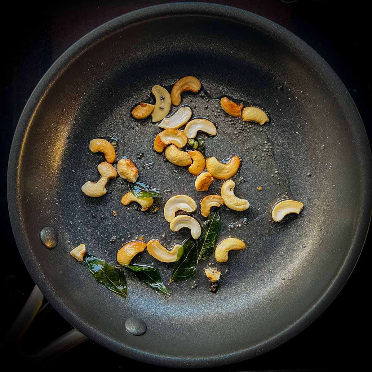 Tempering of mustard seeds, curry leaves, and cashews in a small frying pan.