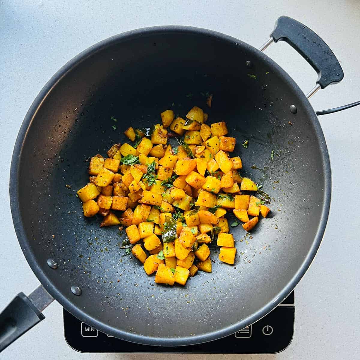 Cooked potato fry topped with cilantro in the frying pan.