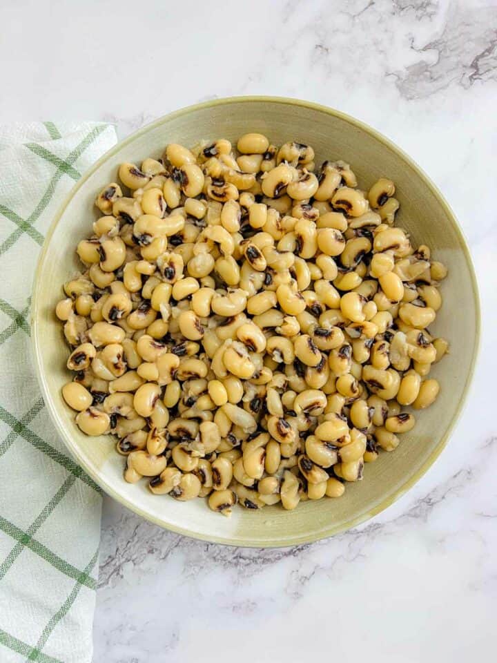 A brown bowl of cooked black-eyed peas on a marble surface.