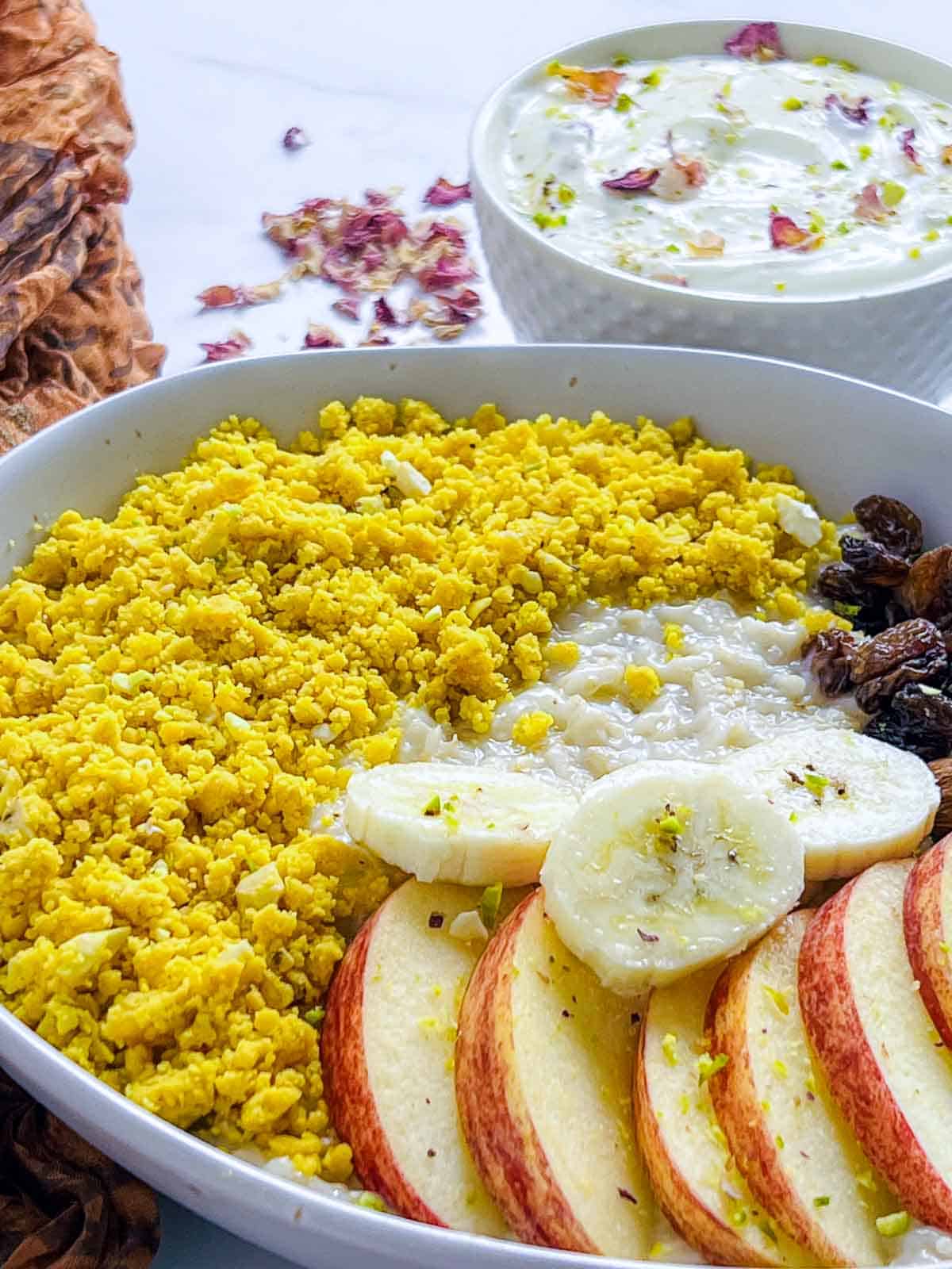 Bowl of assembled oatmeal topped with besan laddu crumble, dried fruits, nuts, and fresh fruits.