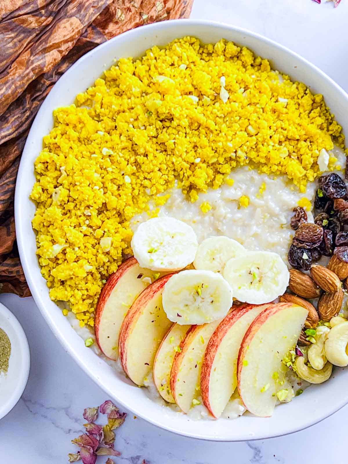 Assembling oatmeal bowl with fruits, nuts, crumble, and oat.