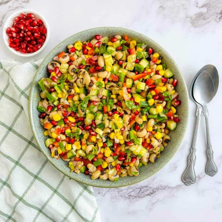 Black-eyed peas salad in a green bowl with spoons in the background.