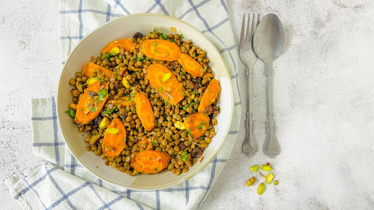 Lentil and carrot salad in a white bowl with spoon in the background.