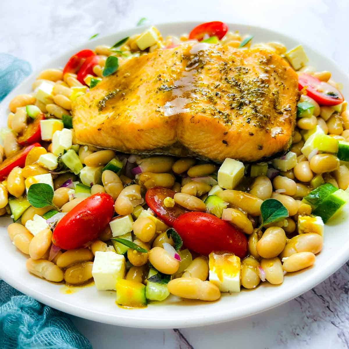 Salmon fillet placed on top of beans and drizzled with dressing.