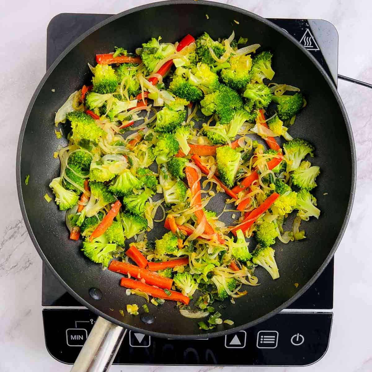 Sauteed broccoli and bell peppers with aromatics in the frying pan.