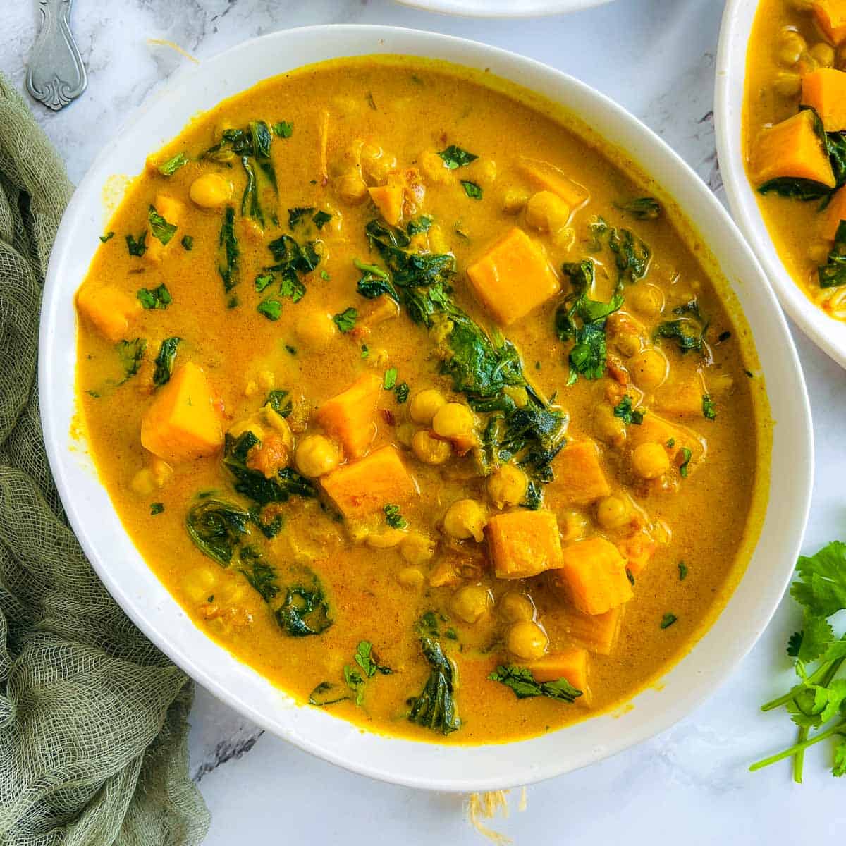 Sweet potato chickpea curry in a white bowl with fresh cilantro in the background.