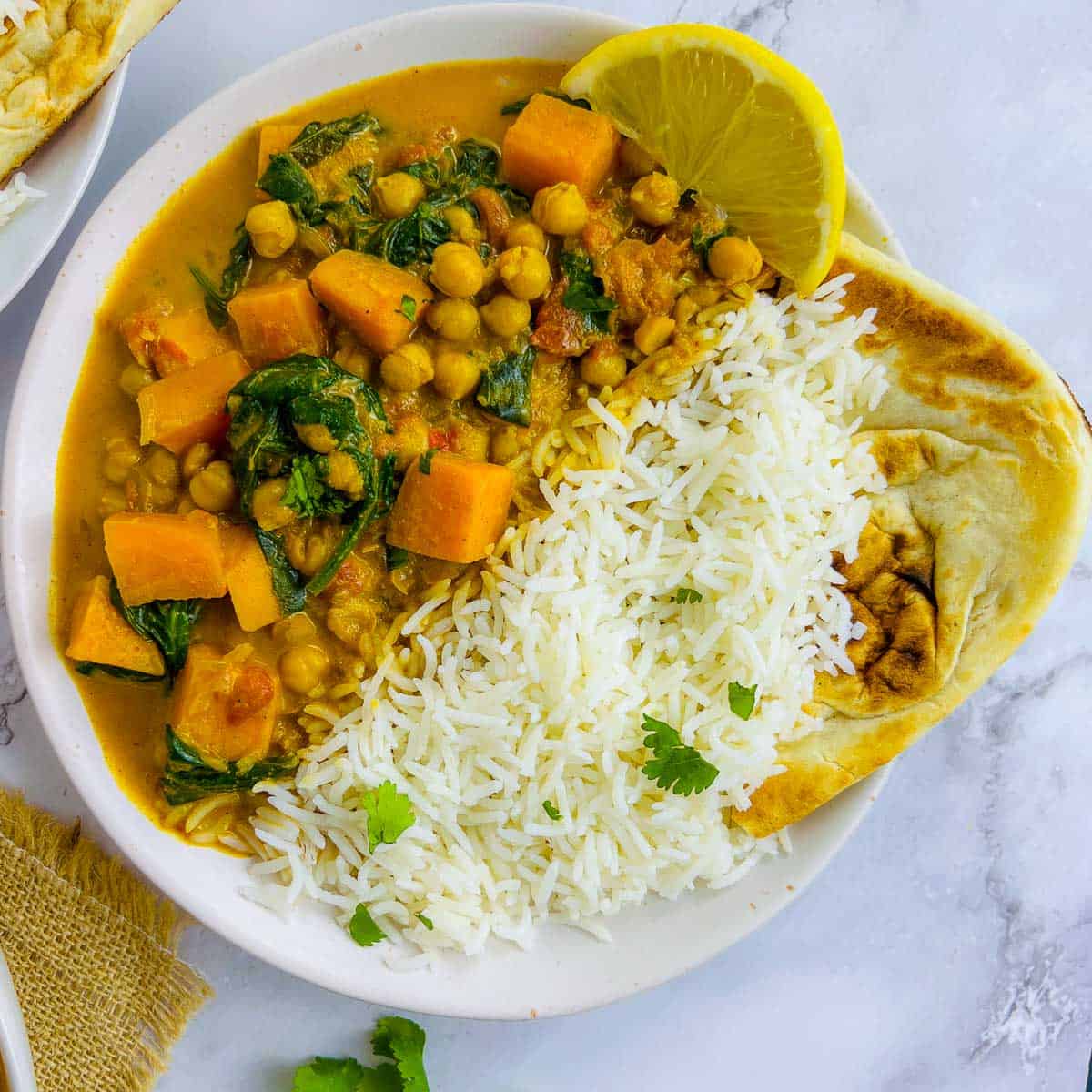 Sweet potato chickpea curry served with rice and naan on a white plate.