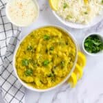 Zucchini dal in a white bowl garnished with cilantro and lemon wedges.