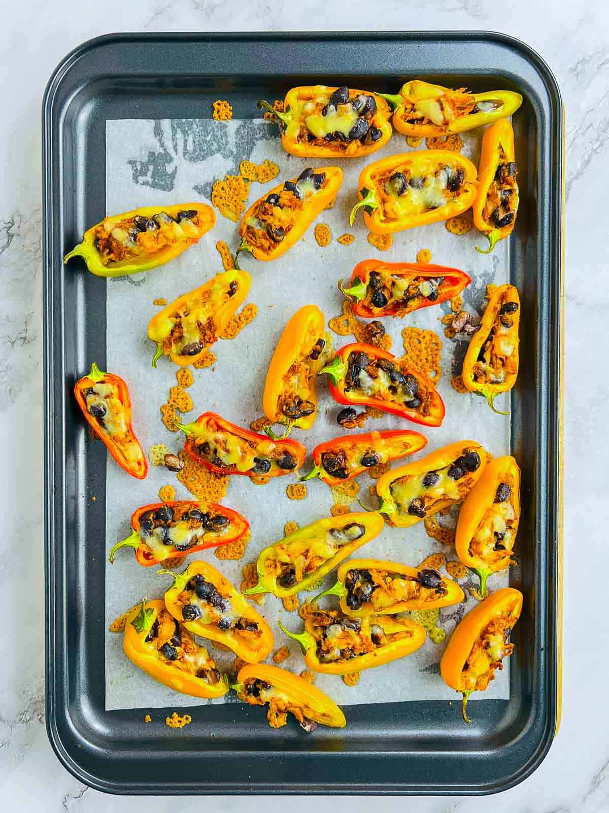 Baked peppers topped with cheese on a baking sheet.