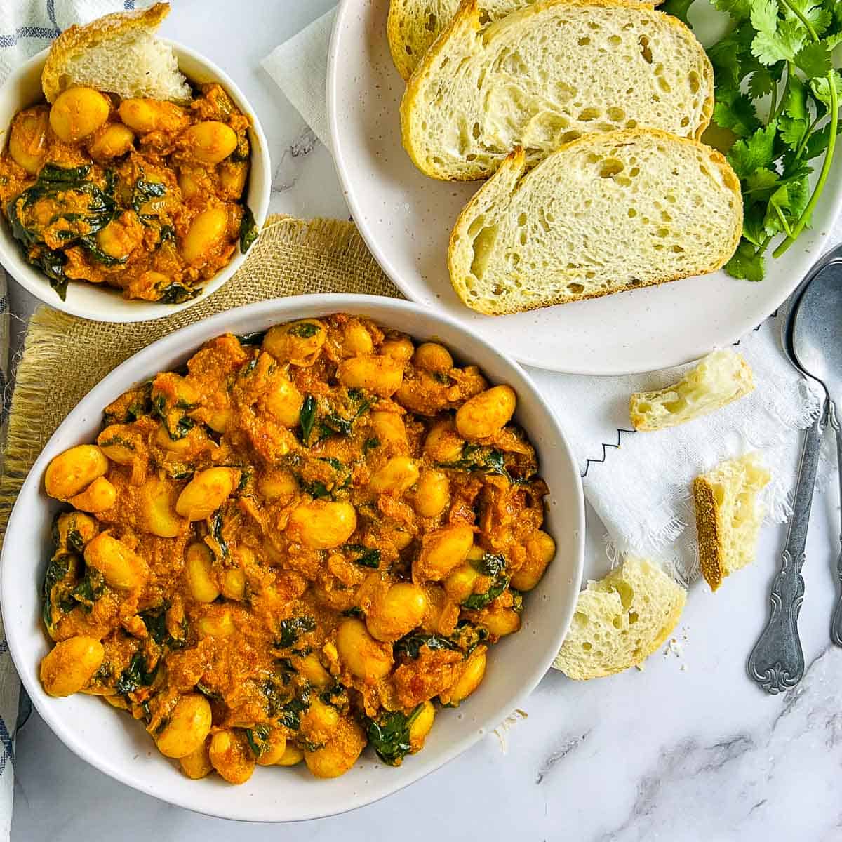 Curried butter beans in a white bowl with bread in the background.