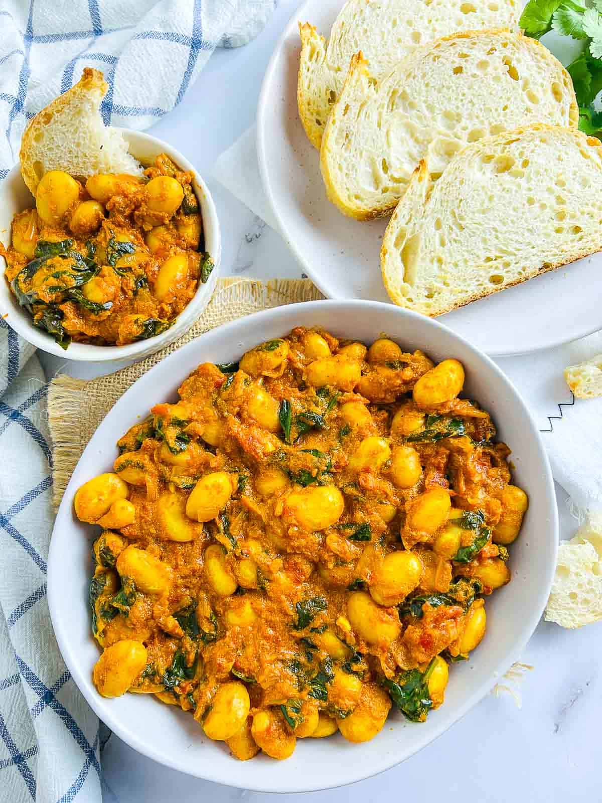 Curried butter beans in a white bowl served with crusty bread and garnished with cilantro.