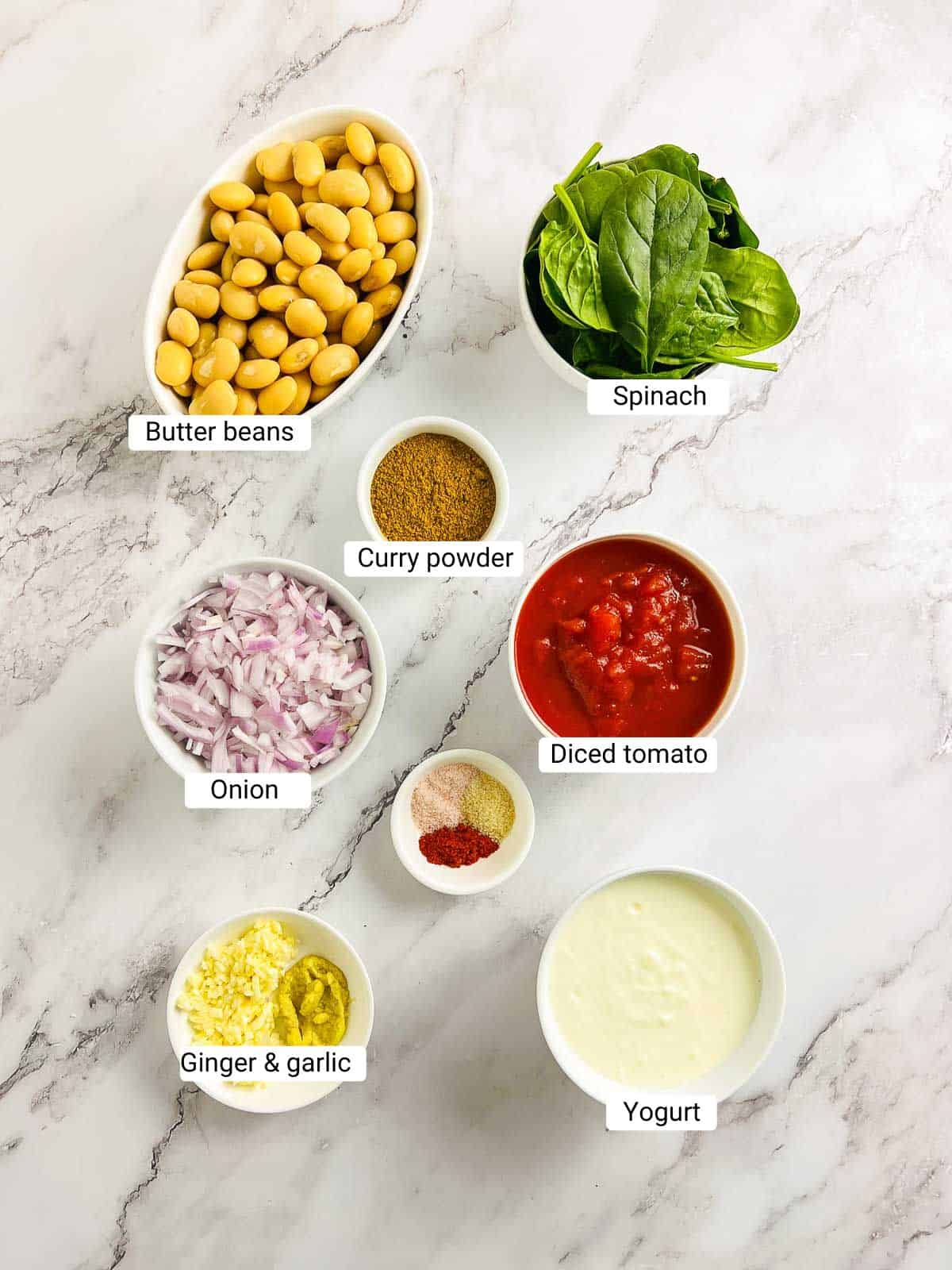 Ingredients to make curried butter beans on a marble surface.