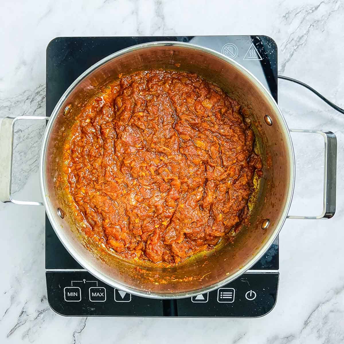 Cooked onion, tomatoes, and spices in a large pot.