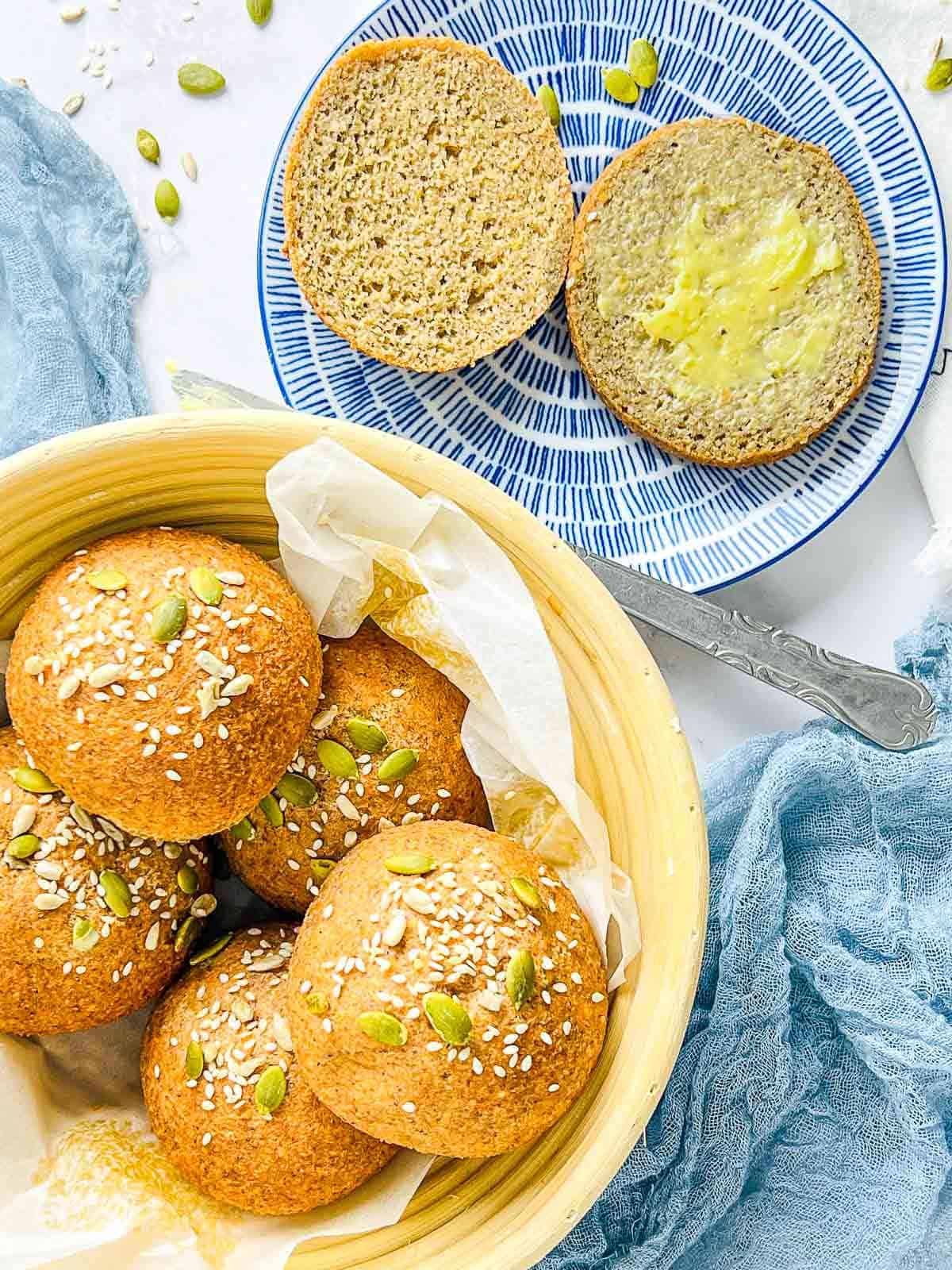 Lentil bread rolls in a basket with on sliced bread roll on a blue plate.