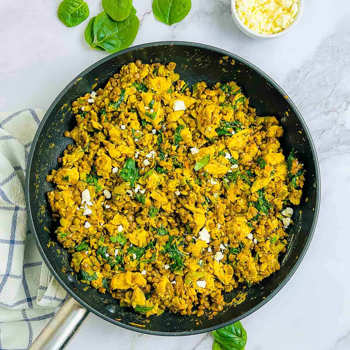 Lentils and eggs breakfast scramble in a skillet with feta cheese in the background.