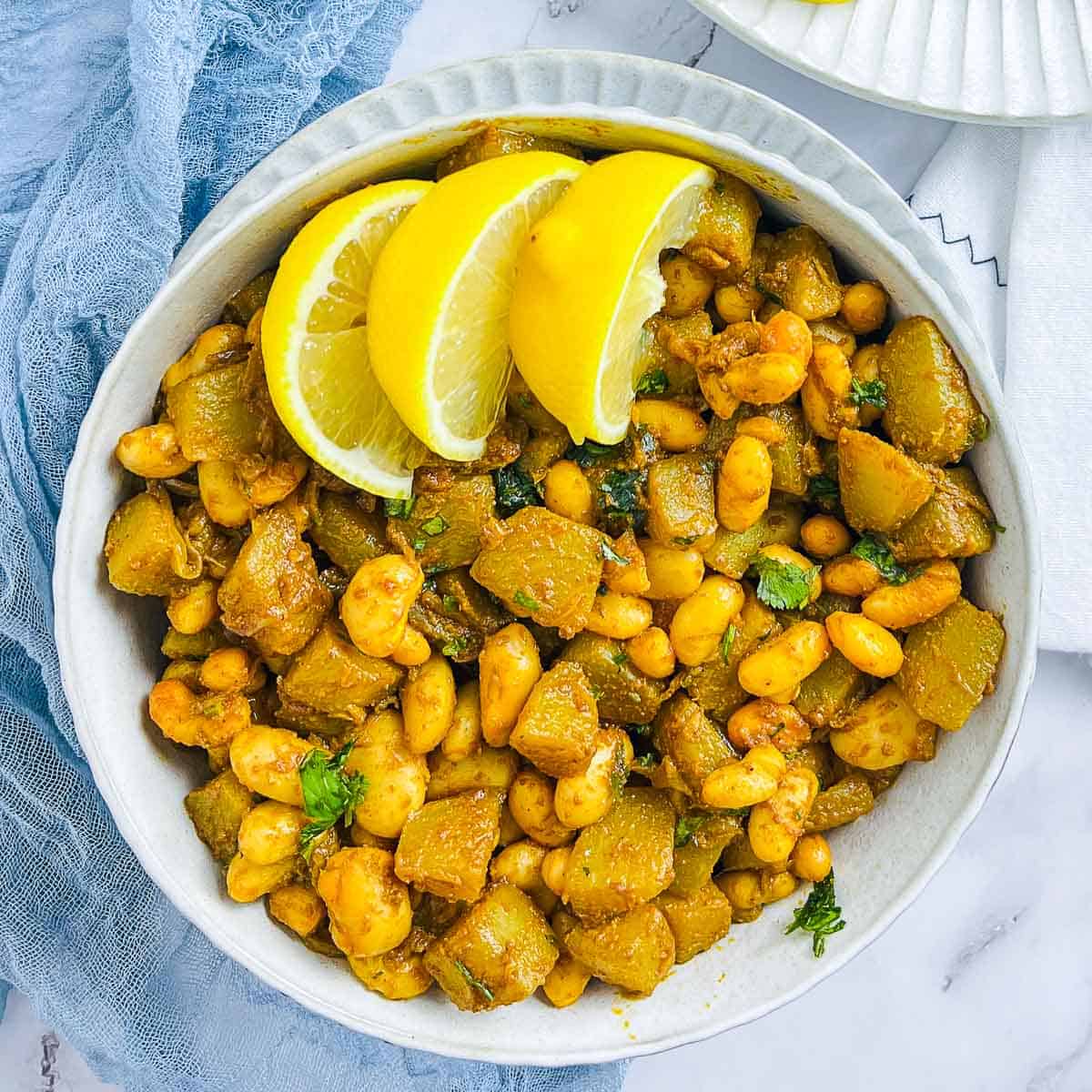 Pan-fried chanyote squash and white beans in a white bowl topped with lemon wedges.