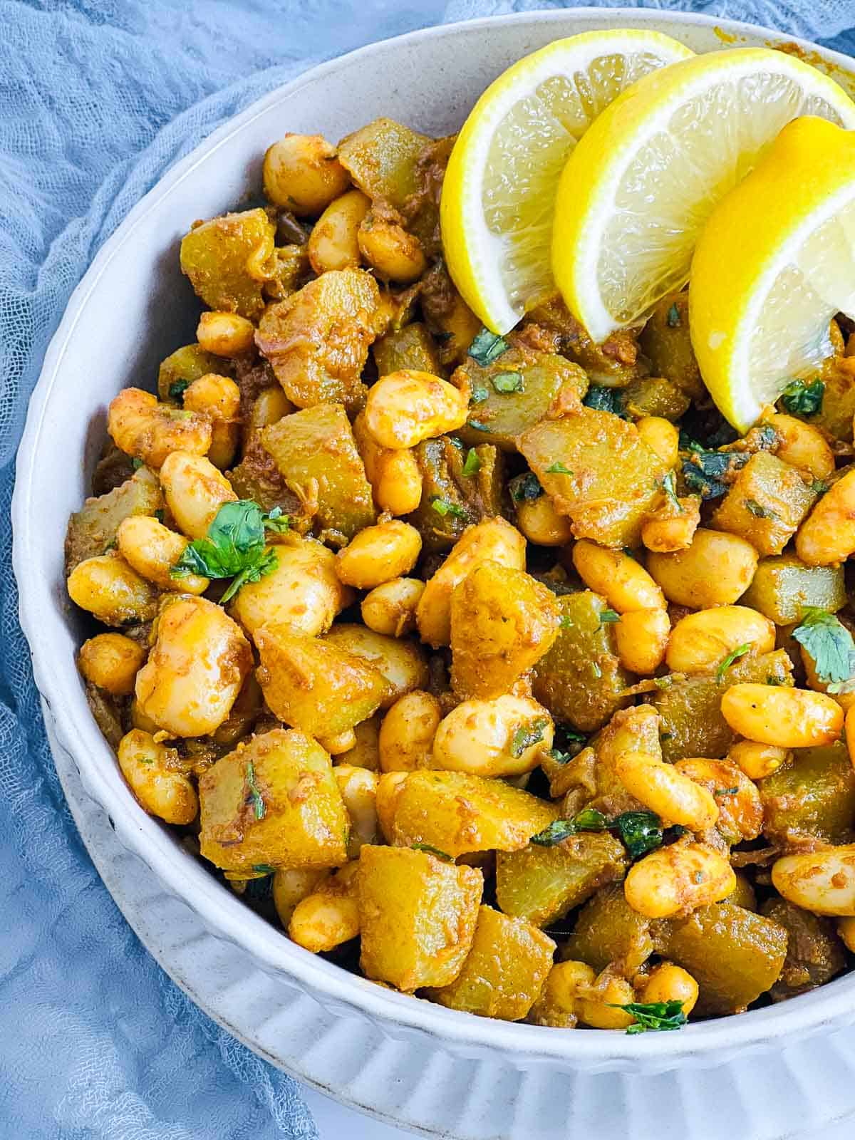 A bowl of pan-fried chayote squash and white beans topped with lemon wedges.