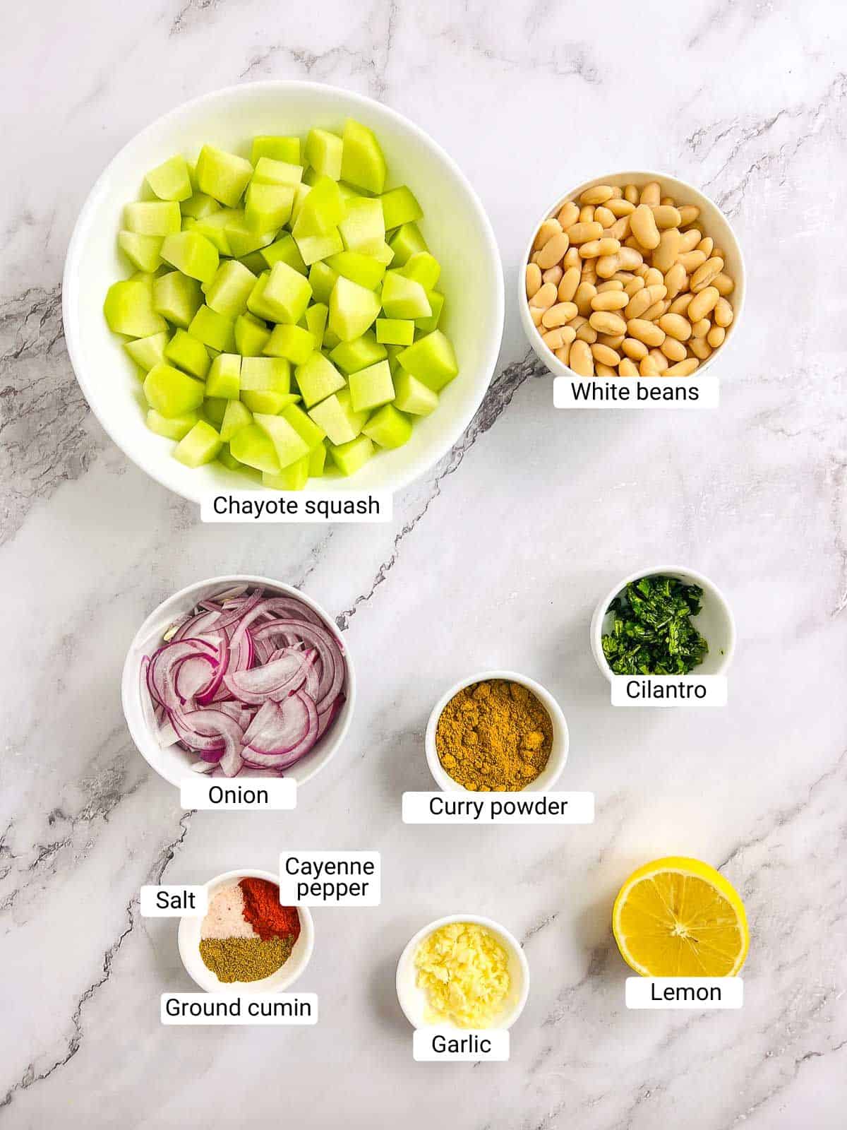 Ingredients to make pan-fried chayote squash and white beans on a marble surface.