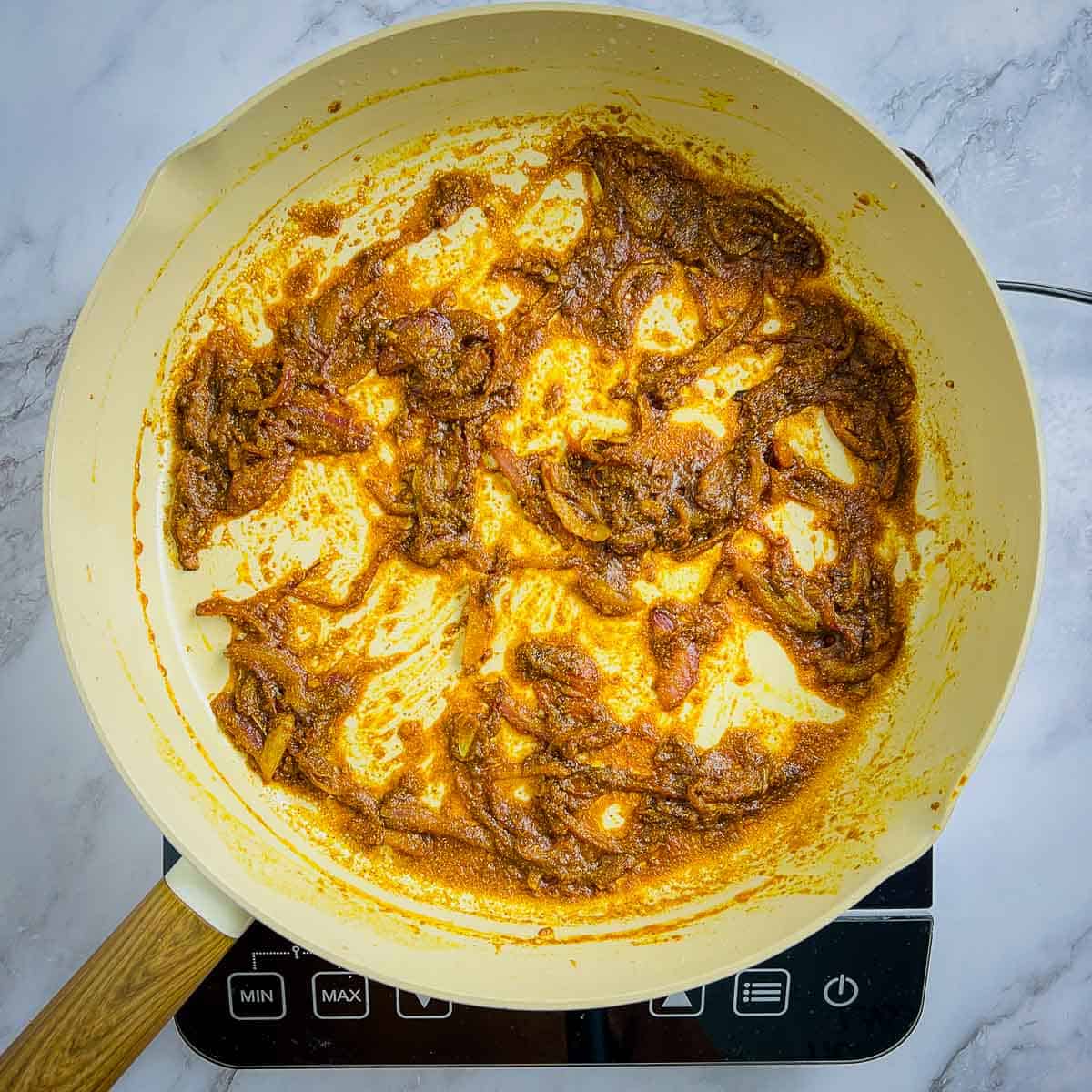 Cooked onion and spice masala in a frying pan.