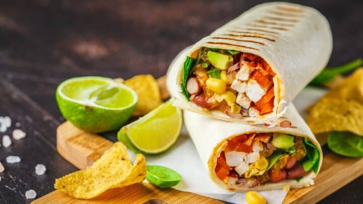 Burrito on a wooden board with line wedges in the background.