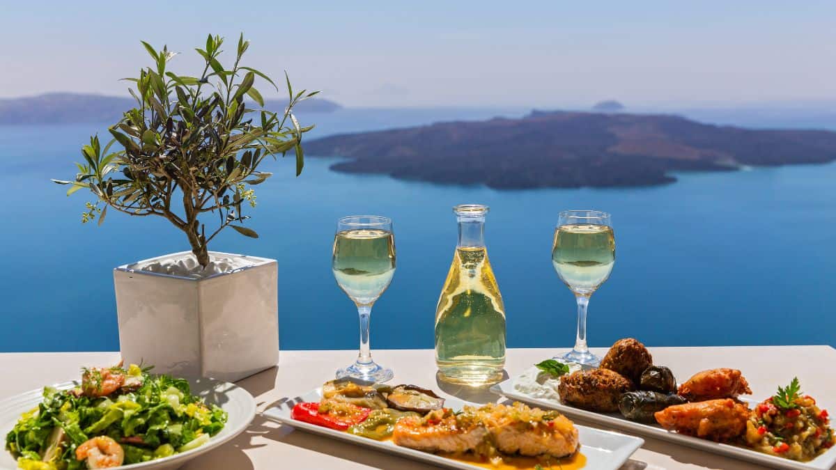 Wine glasses and bottle along with food near a lake.