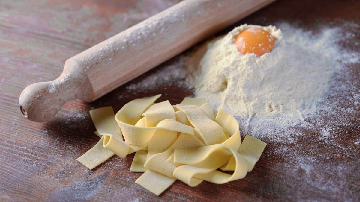 Pappardelle pasta with flour and egg in the background.