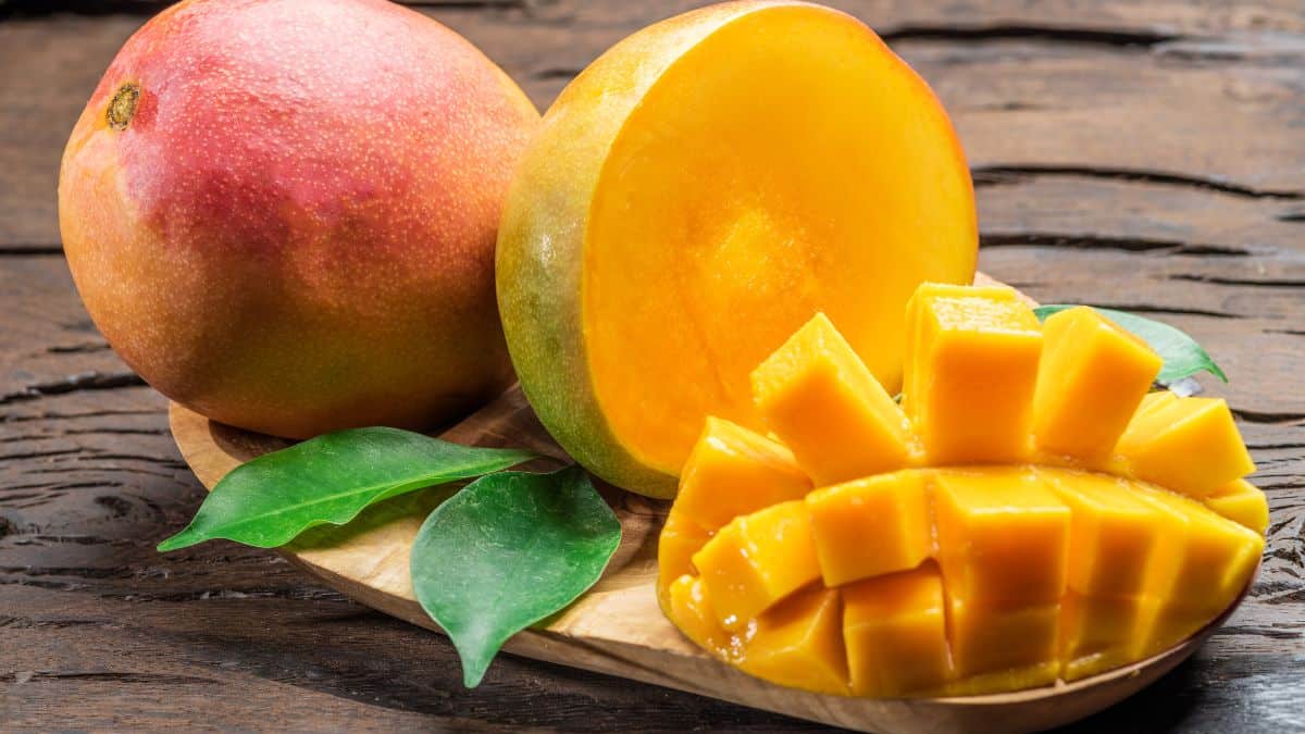 Whole and sliced mango on a wooden board.