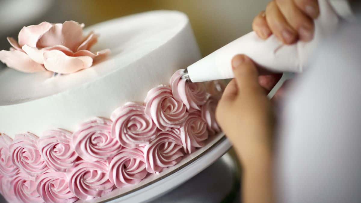 Person frosting cake using a piping bag.