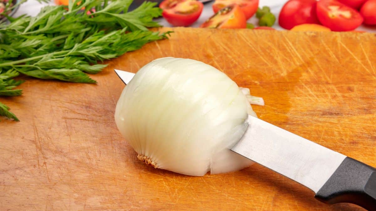 Onion being cut on a wooden board.