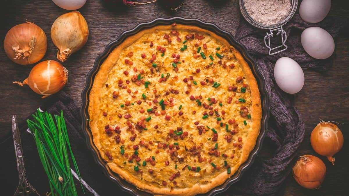 Onion tart on a black surface with onions in the background.