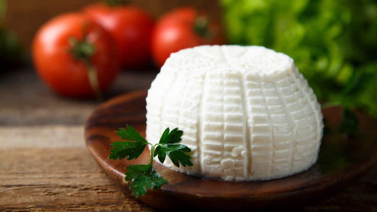 Ricotta cheese on a wooden plate with tomatoes in the background.