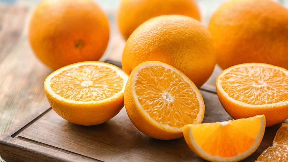 Whole and cut oranges on a wooden board.