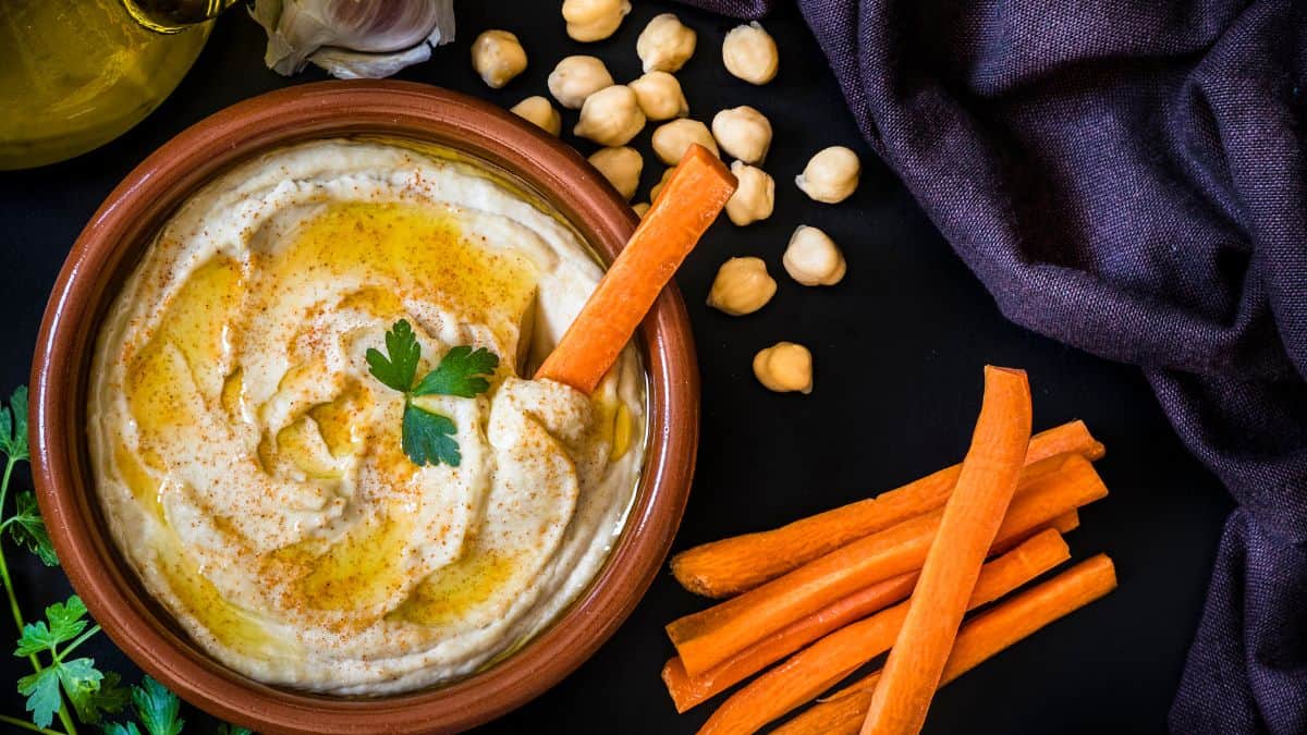 Hummus in a bowl with a carrot stick dipped into it.