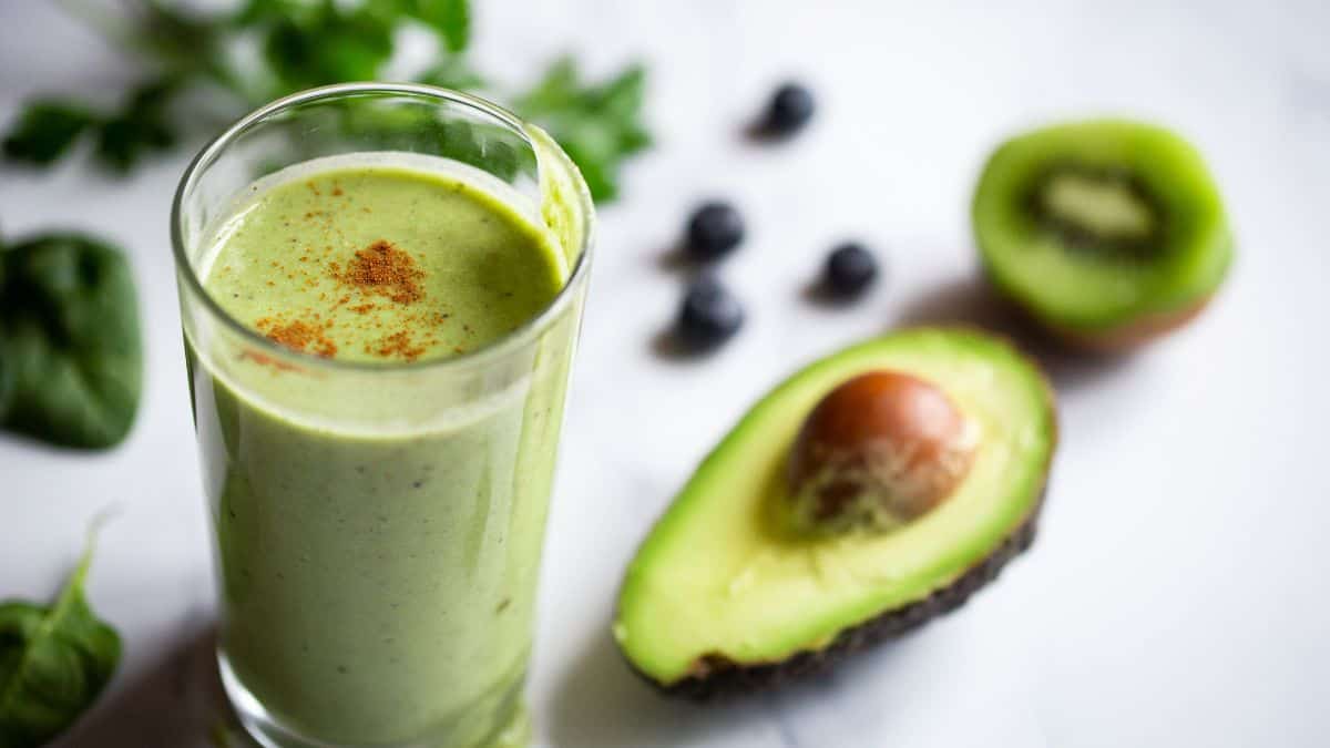 Green smoothie with avocado and kiwi in the background.