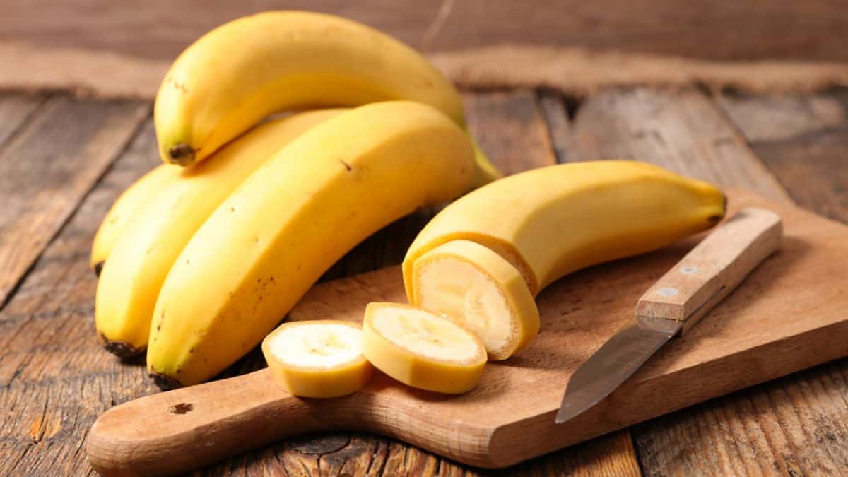 Whole and cut banana on a wooden board.