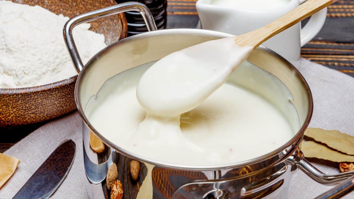 Bechamel sauce in a steel pot with wooden handle inside.