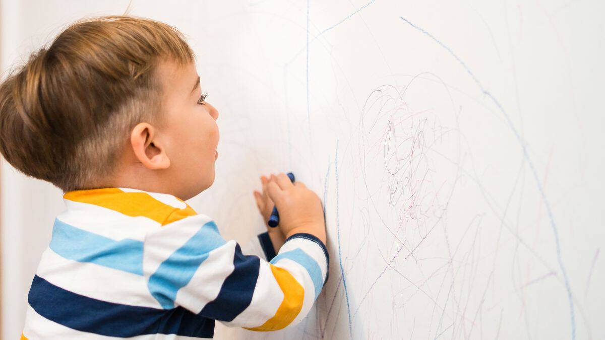 Kid drawing on a wall with crayins.