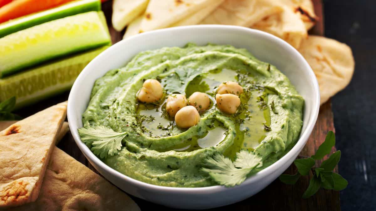 A bowl of cilantro hummus served with dippers.