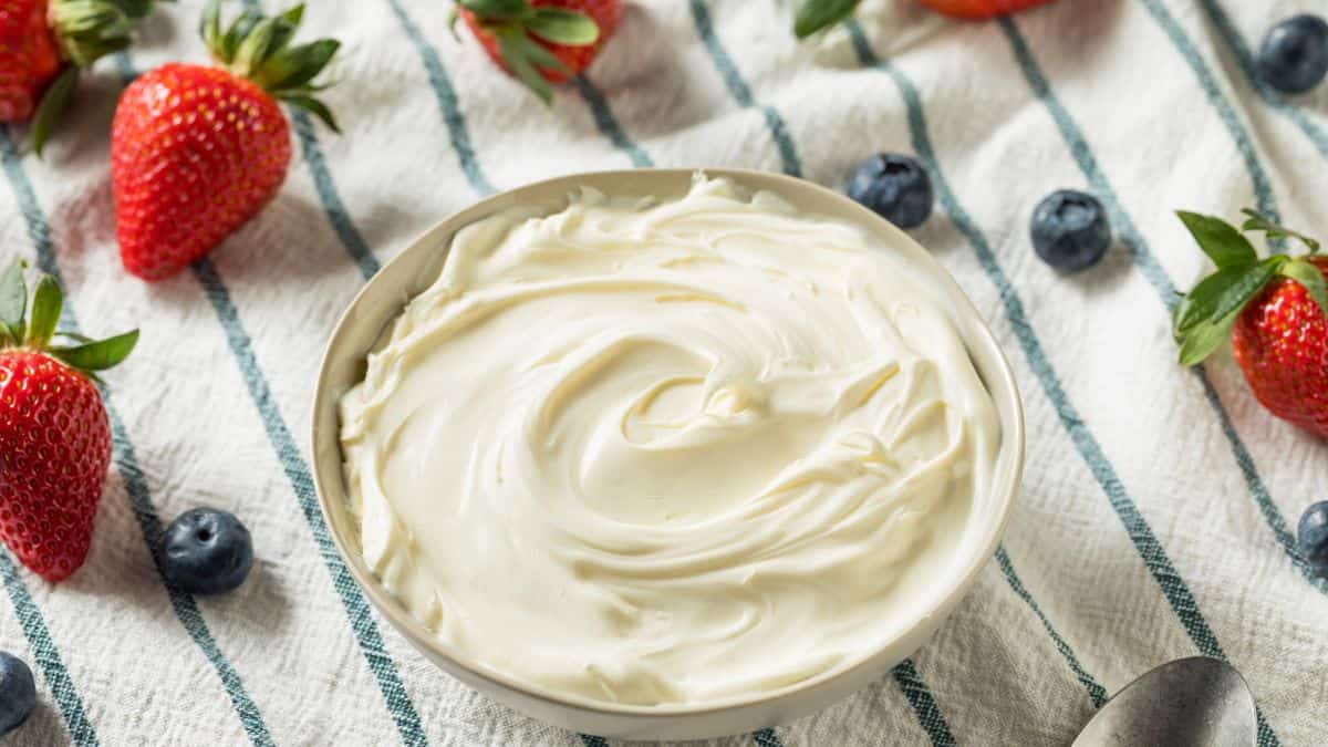 A bowl of mascarpone cheese with berries in the background.