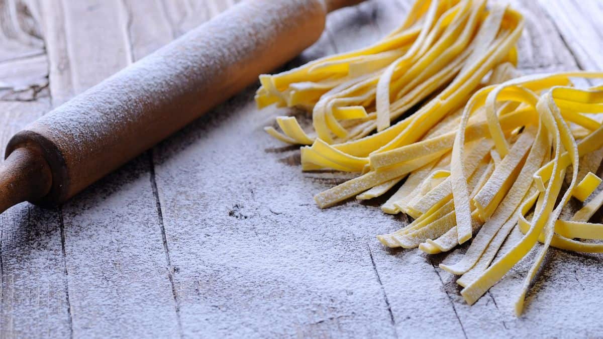 Fresh tagliatelle pasta with a rolling pin in the background.