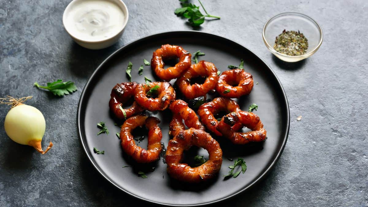 Bacon wrapped onion rings on a black plate.