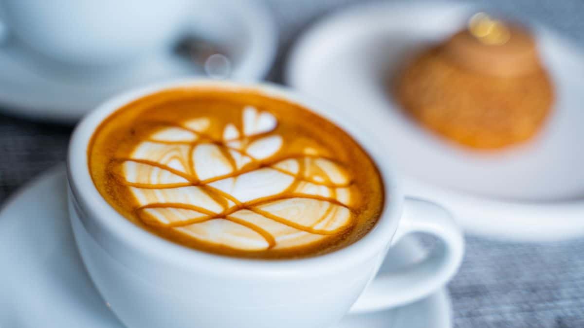 A cup of caramel macchiato with bread in the background.