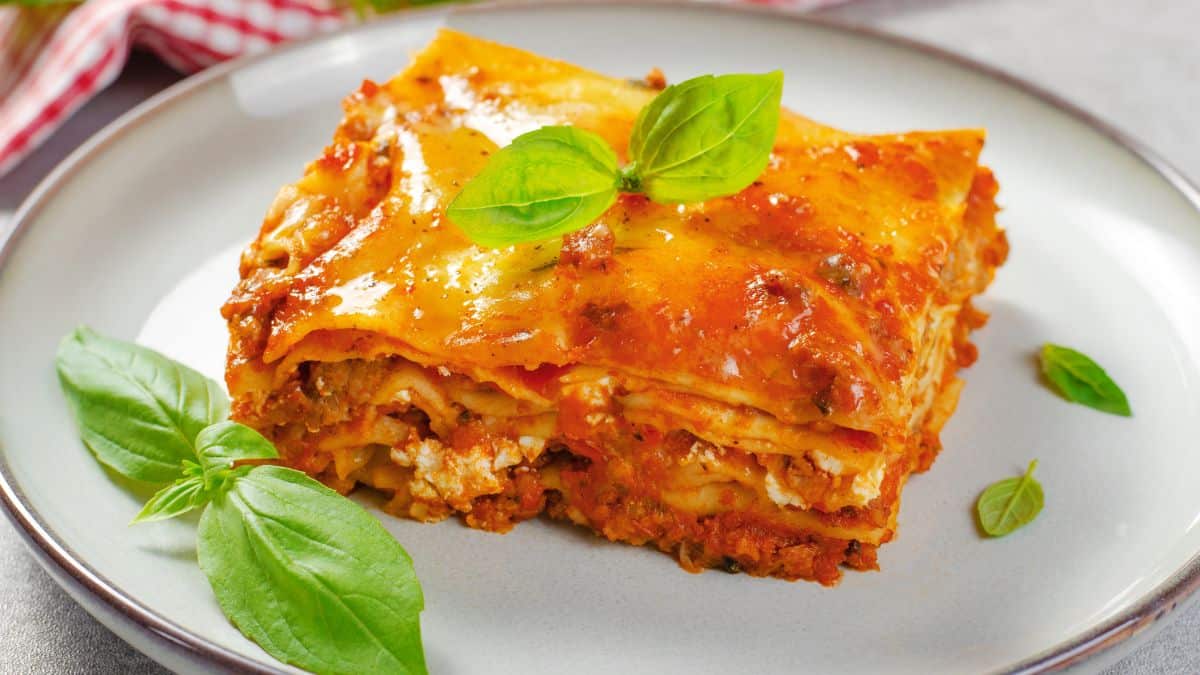 Lasagna on a white plate garnished with basil.