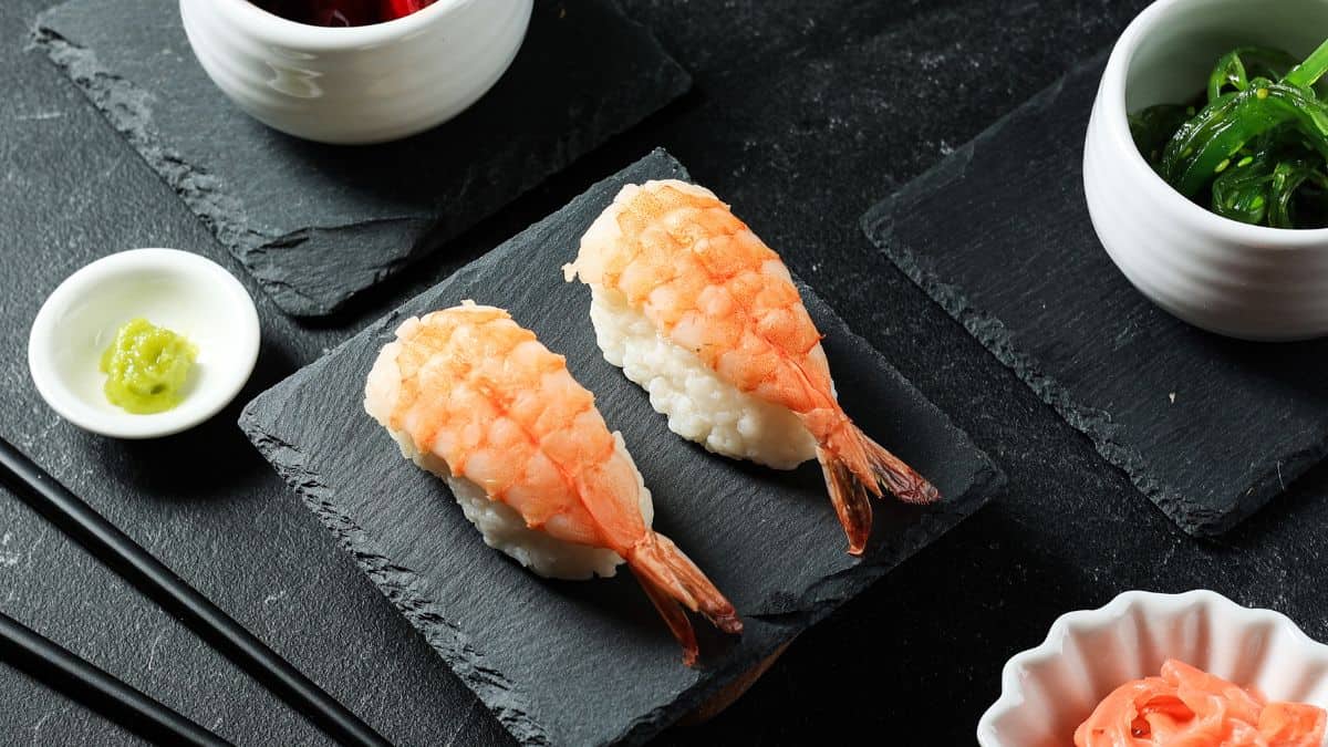 Two pieces og ebi nigiri on a plate with dipping sauces in the background.