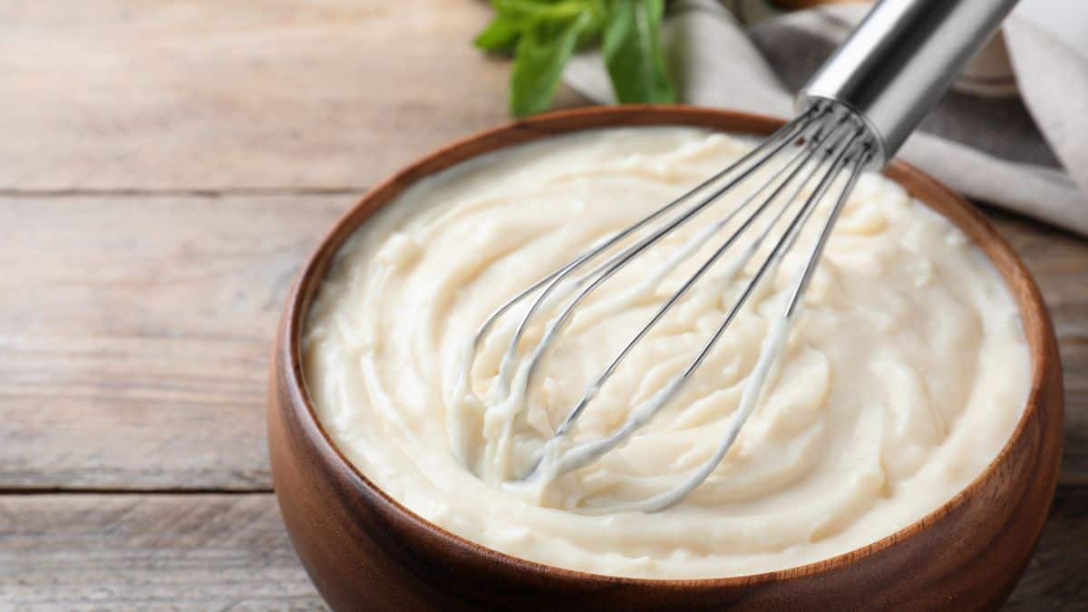 Heavy cream in a browl bowl with a whisk on the top.