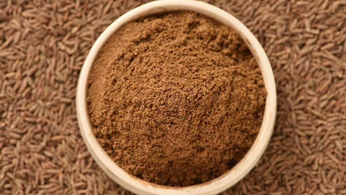 Ground cumin in a bowl with cumin seeds in the background.