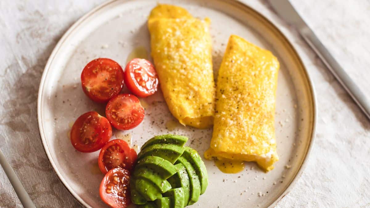 French omelet on a white plate with tomato and avocado.