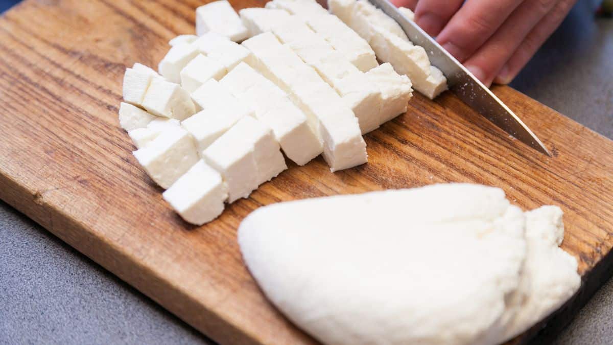 Paneer cubes and block on a wooden board.