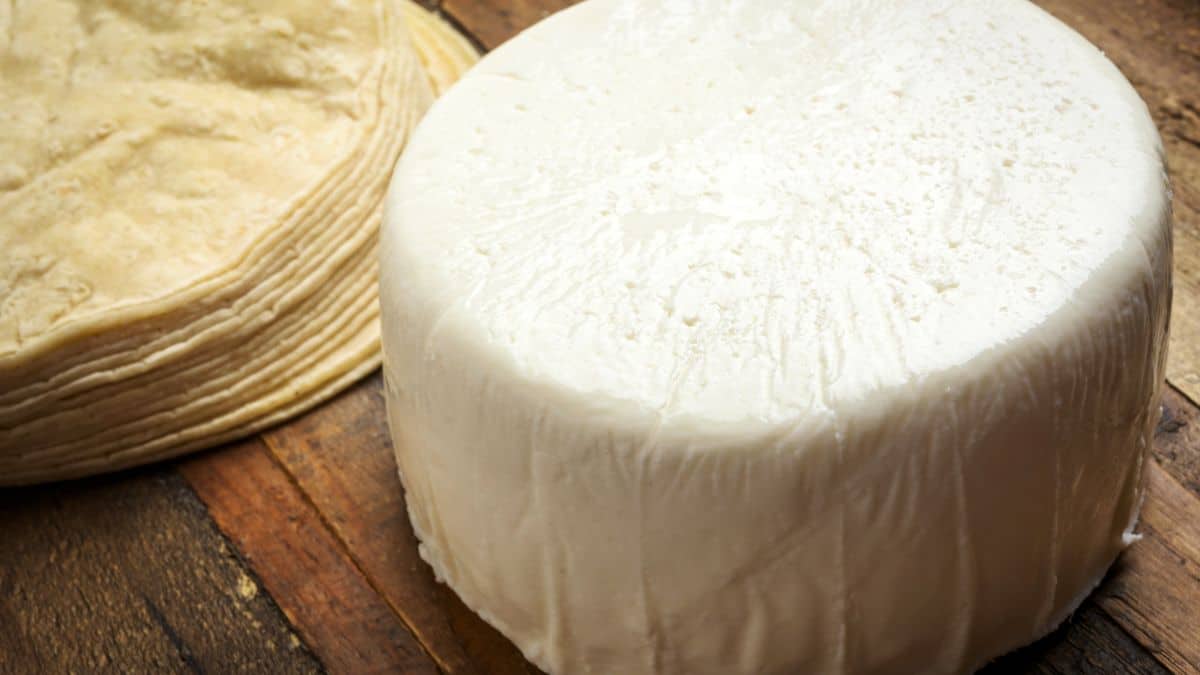 A block of queso fresco with tortillas in the background.